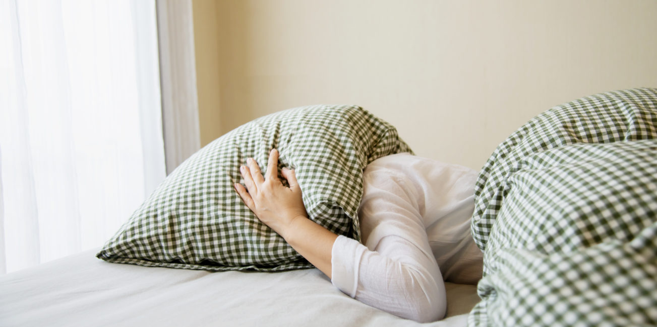 Femme la tête sous un oreiller cherchant son sommeil.