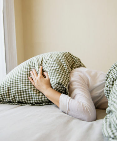 Femme la tête sous un oreiller cherchant son sommeil.