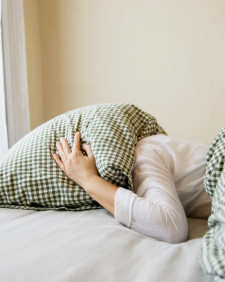 Femme la tête sous un oreiller cherchant son sommeil.